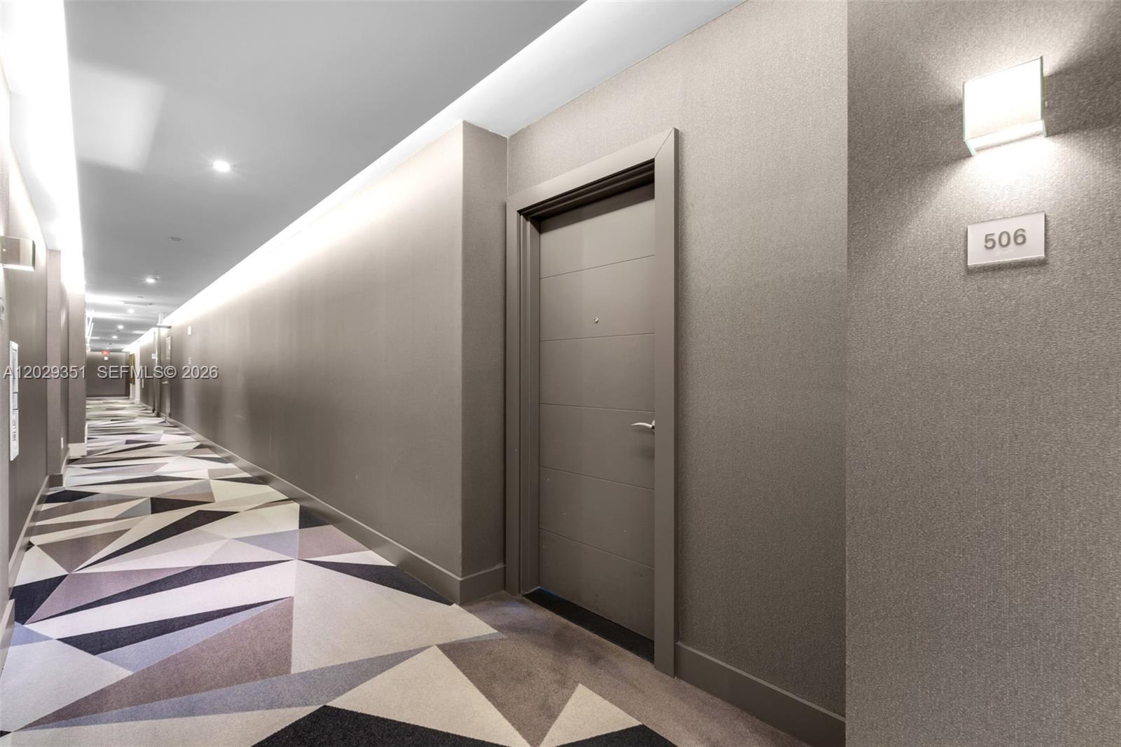 A modern hotel hallway features a geometric patterned carpet, gray walls, and door number 506 — 17111 BISCAYNE BL # 506, North Miami Beach FL 33160, NORTH MIAMI BEACH, FL