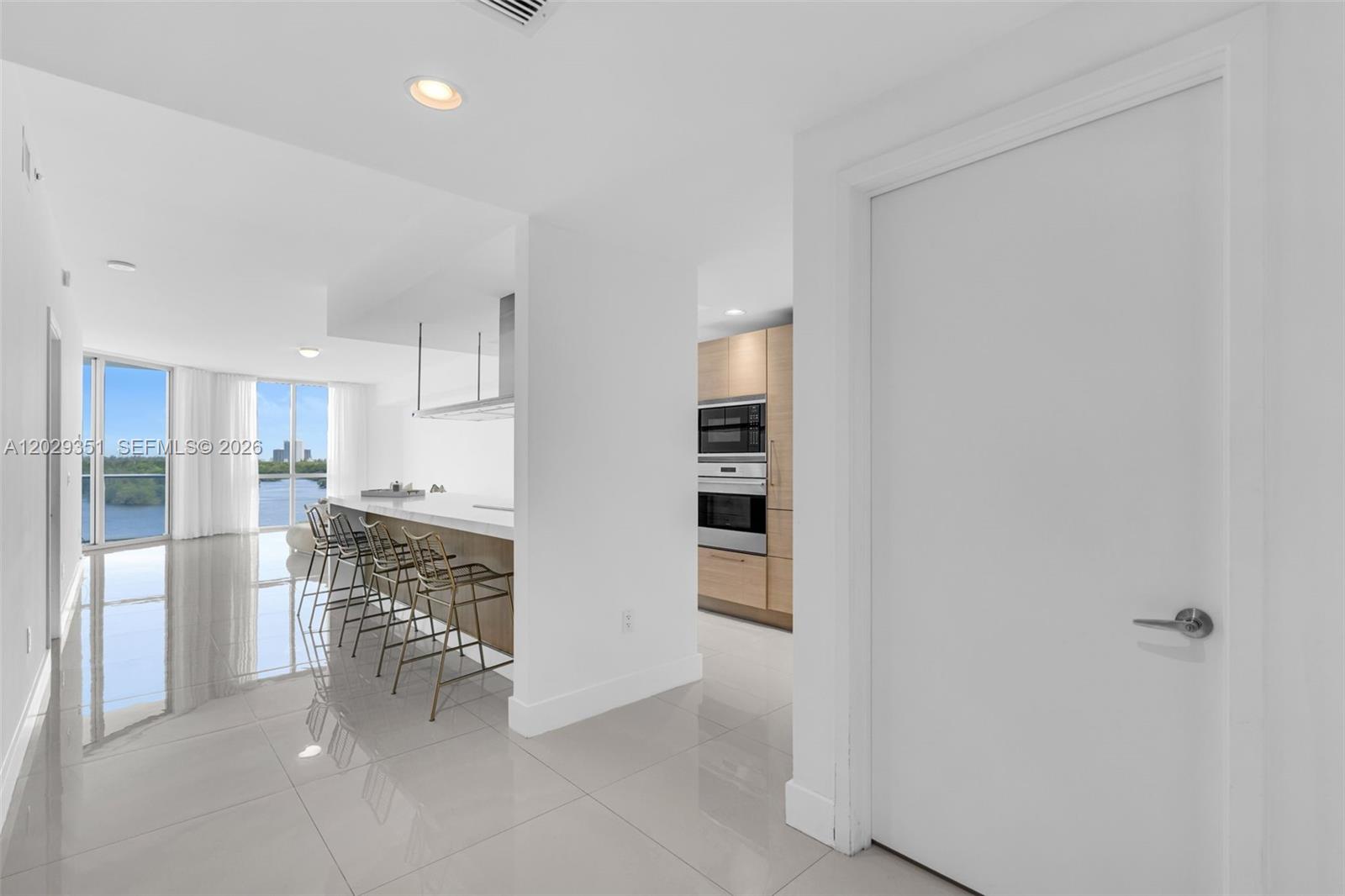 A modern kitchen features a breakfast bar, light wood cabinetry, and large floor-to-ceiling windows — 17111 BISCAYNE BL # 506, North Miami Beach FL 33160, NORTH MIAMI BEACH, FL