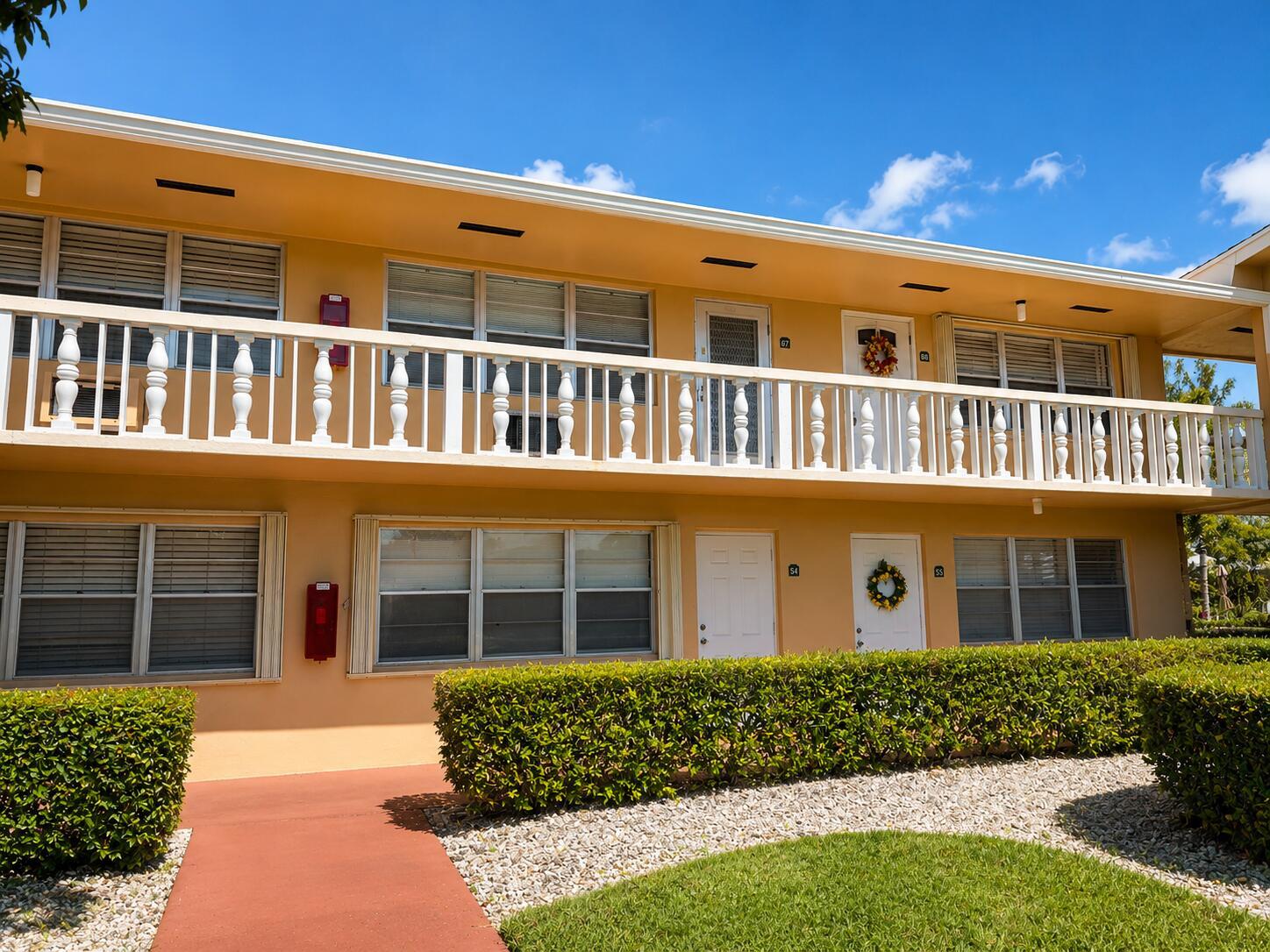 A two-story apartment building features a yellow exterior, a white balcony railing, and landscaped hedges — 67 Camden C, West Palm Beach FL 33417, WEST PALM BEACH, FL