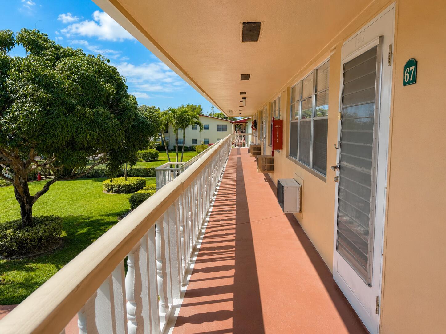 An exterior walkway with a white railing overlooks a grassy courtyard with trees — 67 Camden C, West Palm Beach FL 33417, WEST PALM BEACH, FL