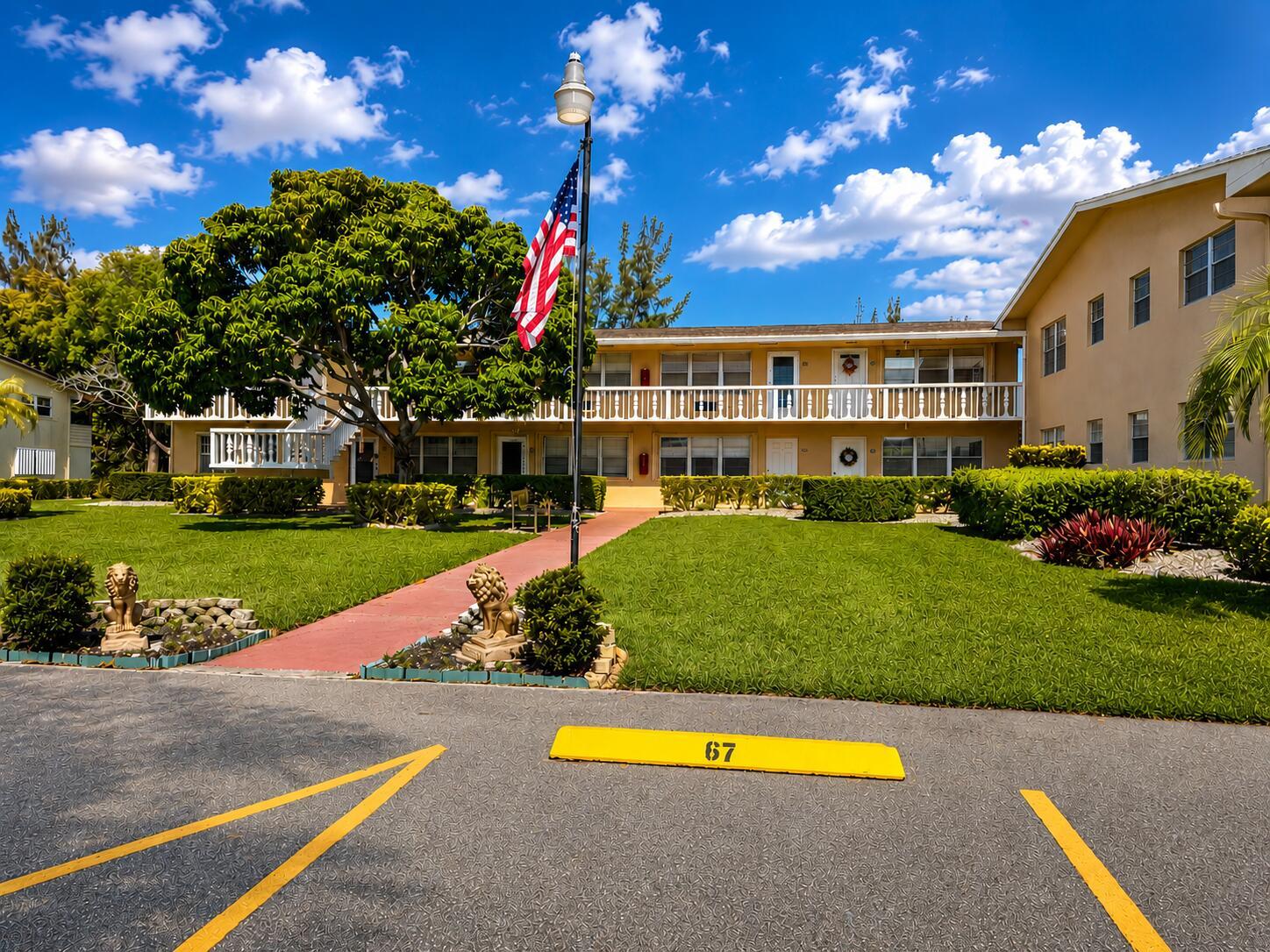 A two-story apartment building with a lawn, American flag, and parking space number 67 — 67 Camden C, West Palm Beach FL 33417, WEST PALM BEACH, FL