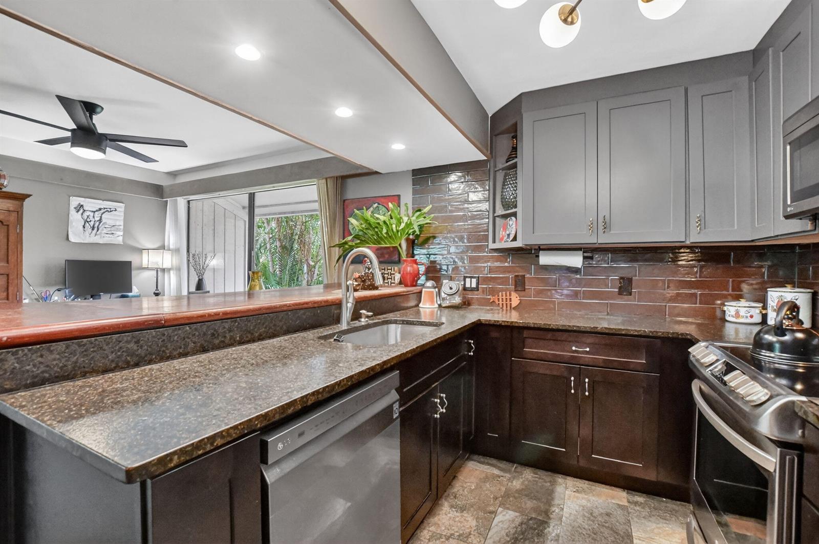 A kitchen features dark wood cabinets, granite countertops, a brown tile backsplash, and stainless appliances — 6957 Rain Forest Drive, Boca Raton FL 33434, BOCA RATON, FL