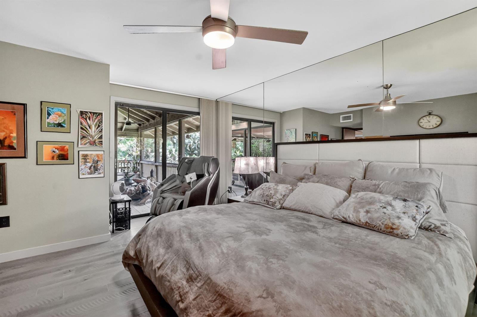 A bedroom features a large bed, mirrored wall, ceiling fan, and sliding doors to a deck — 6957 Rain Forest Drive, Boca Raton FL 33434, BOCA RATON, FL