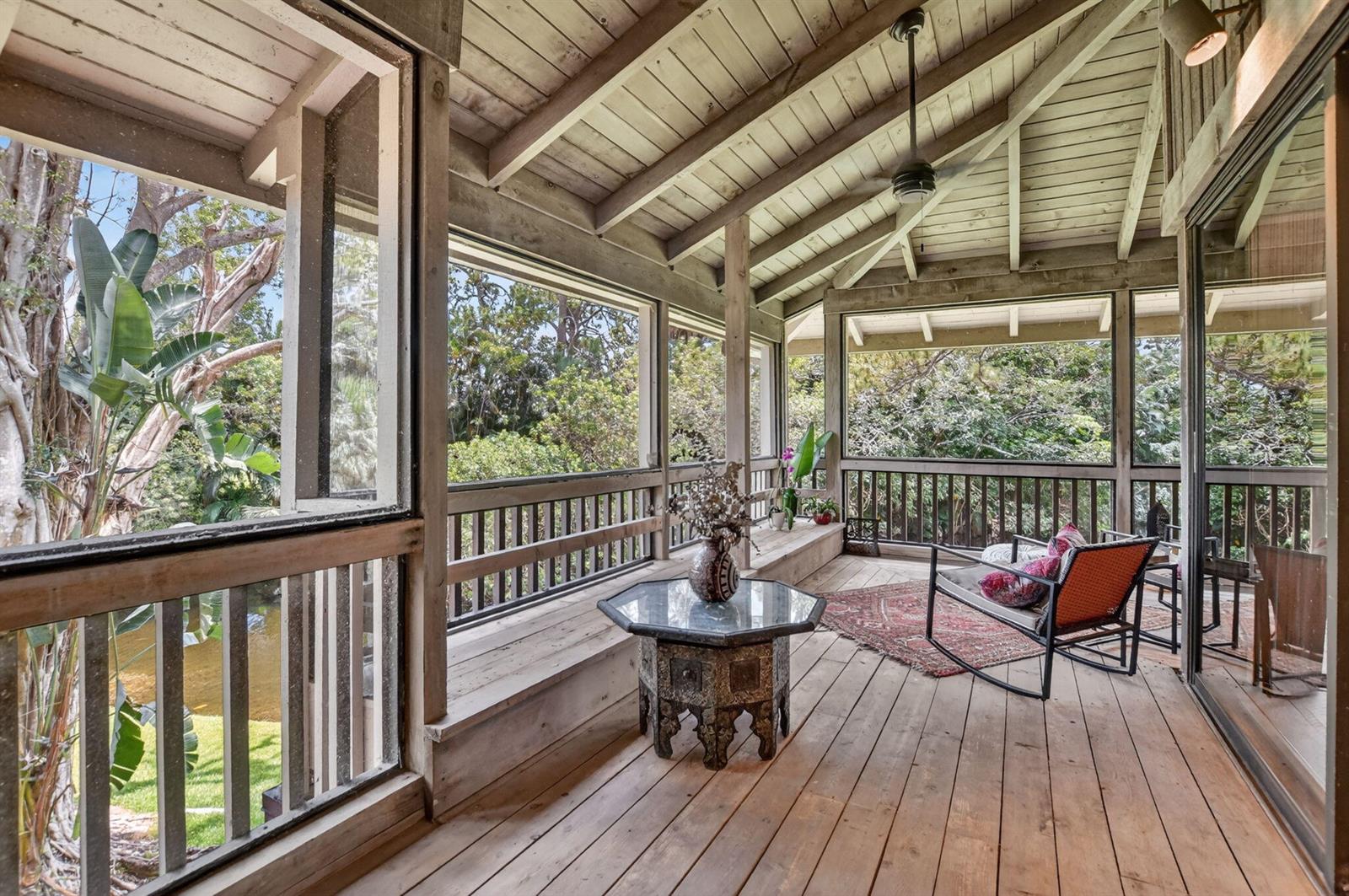 A screened-in wooden porch features a rocking chair, an octagonal table, and views of trees — 6957 Rain Forest Drive, Boca Raton FL 33434, BOCA RATON, FL