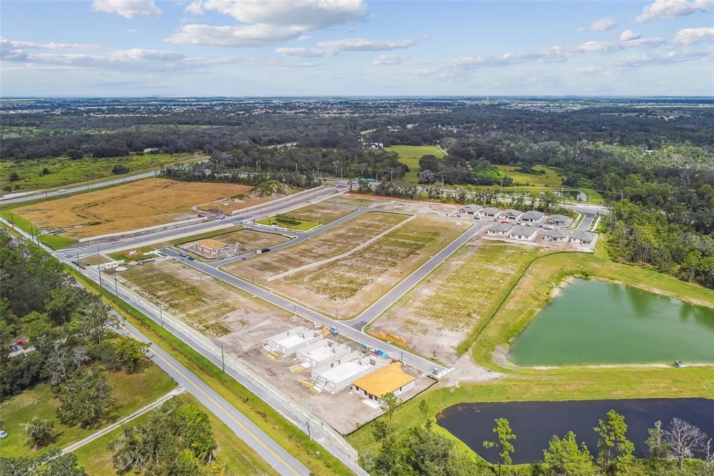An aerial view shows a residential development site with paved roads, construction, and a pond — 2936 BERRY COPPICE PLACE, WIMAUMA, FL