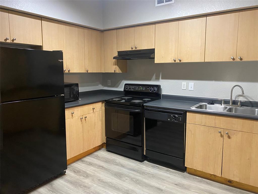 A kitchen features light wood cabinets, black appliances, dark countertops, and light wood-look flooring — 520 S ARMENIA AVENUE UNIT 1228, TAMPA, FL