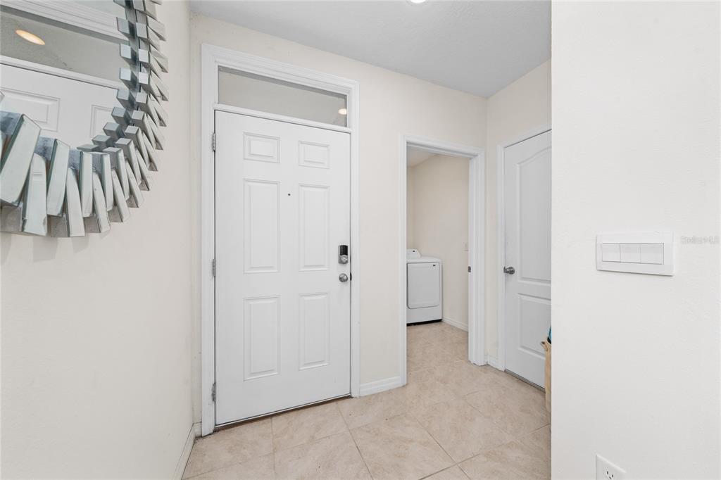An entryway features a white front door, tile flooring, and a doorway to a laundry room — 1107 CASCADE DRIVE, DAVENPORT, FL