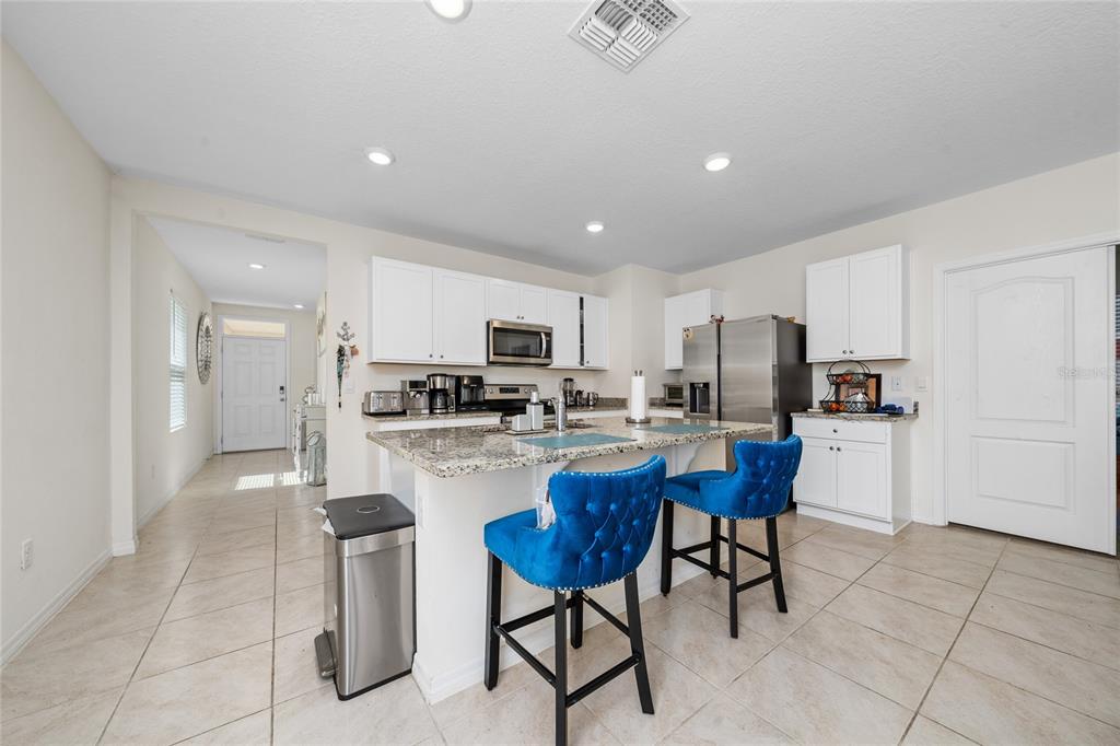 A kitchen features white cabinets, granite countertops, a center island with blue stools, and tile flooring — 1107 CASCADE DRIVE, DAVENPORT, FL