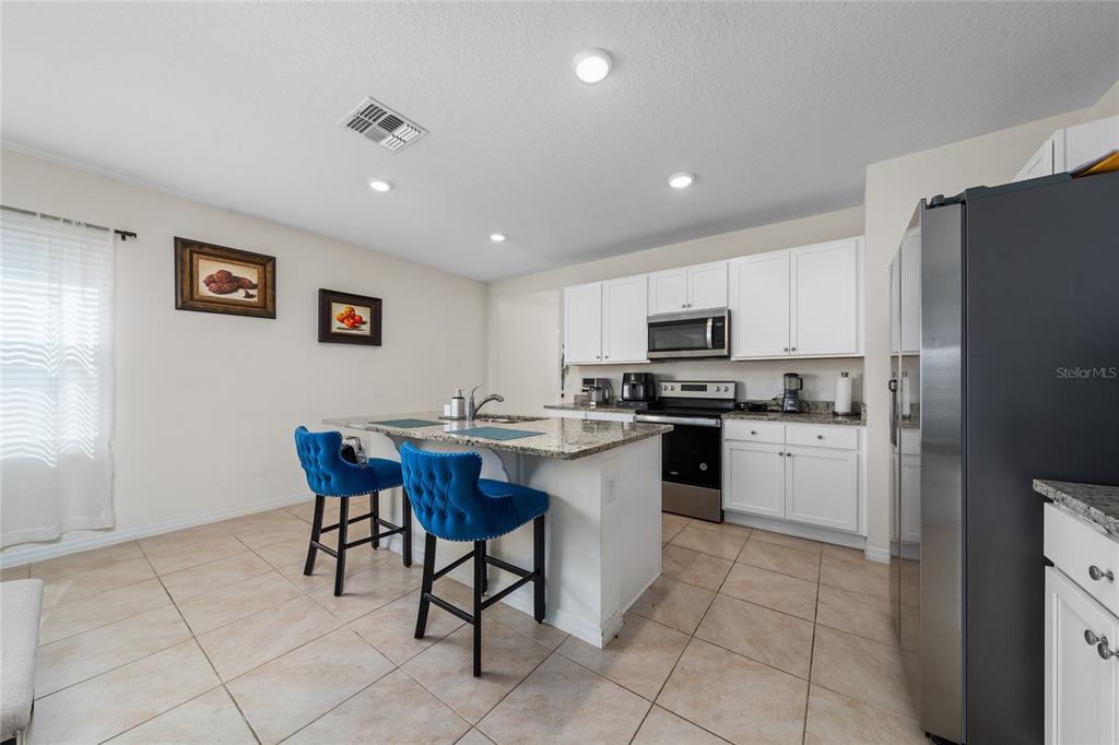 A kitchen features white cabinets, granite countertops, a center island, and two blue bar stools — 1107 CASCADE DRIVE, DAVENPORT, FL