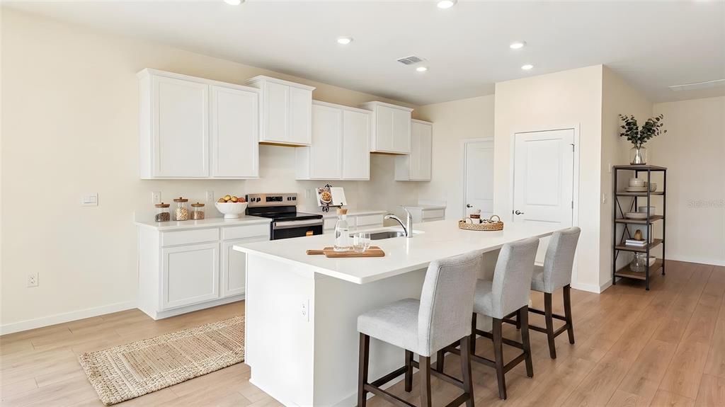 A modern kitchen features white cabinets, a large island with bar seating, and light wood flooring — 4550 NW 39TH STREET ROAD, OCALA, FL