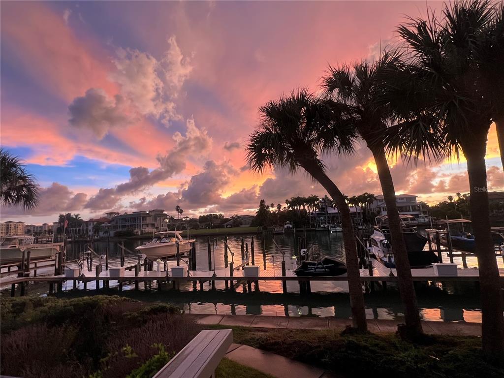 A sunset view over a canal with boat docks, palm trees, and waterfront homes — 910 PINELLAS BAYWAY S UNIT 103, TIERRA VERDE, FL