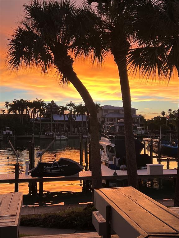 A sunset view over a canal with palm trees, a boat dock, and residential houses — 910 PINELLAS BAYWAY S UNIT 103, TIERRA VERDE, FL