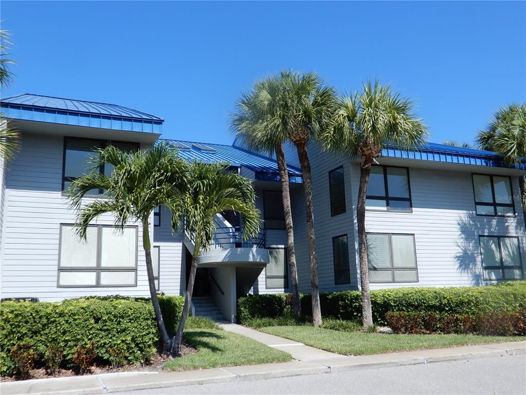 A two-story building with light gray siding, a blue metal roof, and palm trees — 910 PINELLAS BAYWAY S UNIT 103, TIERRA VERDE, FL