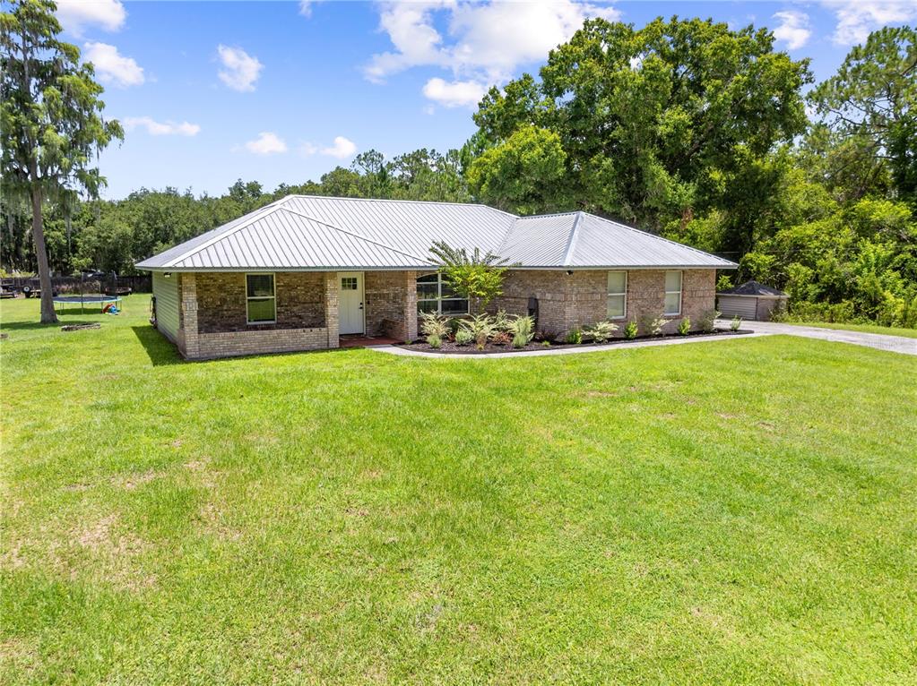 A single-story brick house with a metal roof sits on a large grassy lawn — 3839 LAKEVIEW ACRES RD, ST CLOUD, FL