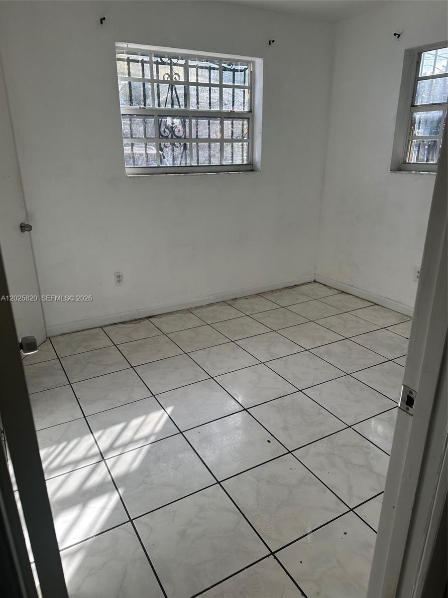 An empty room features white walls, light-colored tile flooring, and two windows with security bars — 7024 NW 6th Ave # 1, Miami FL 33150, MIAMI, FL