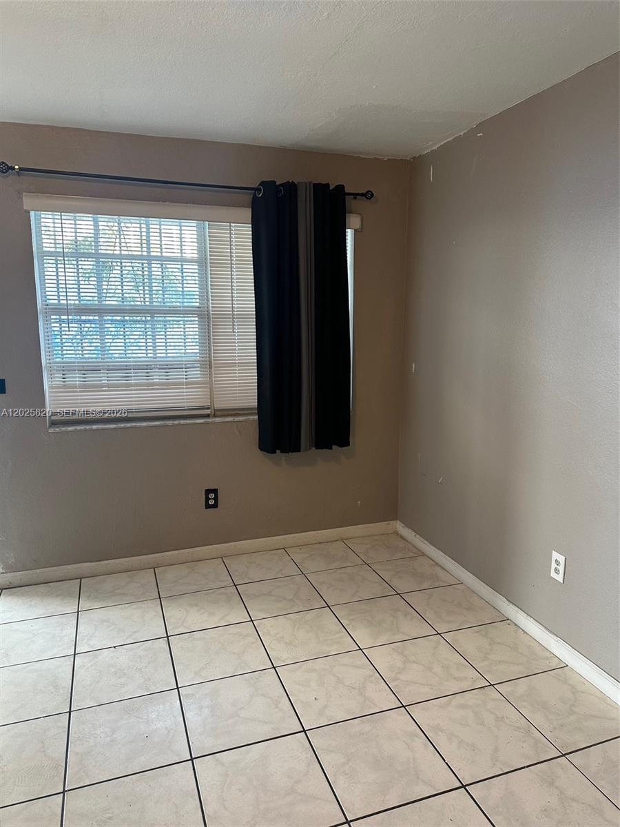 An empty room features beige tile flooring, a window with blinds, and dark curtains — 7024 NW 6th Ave # 1, Miami FL 33150, MIAMI, FL