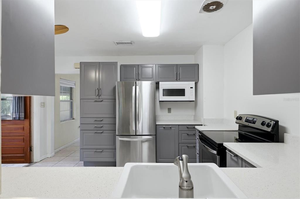 A kitchen features gray cabinets, stainless steel appliances, a white farmhouse sink, and tile flooring — 4003 BOOTH PLACE, SARASOTA, FL
