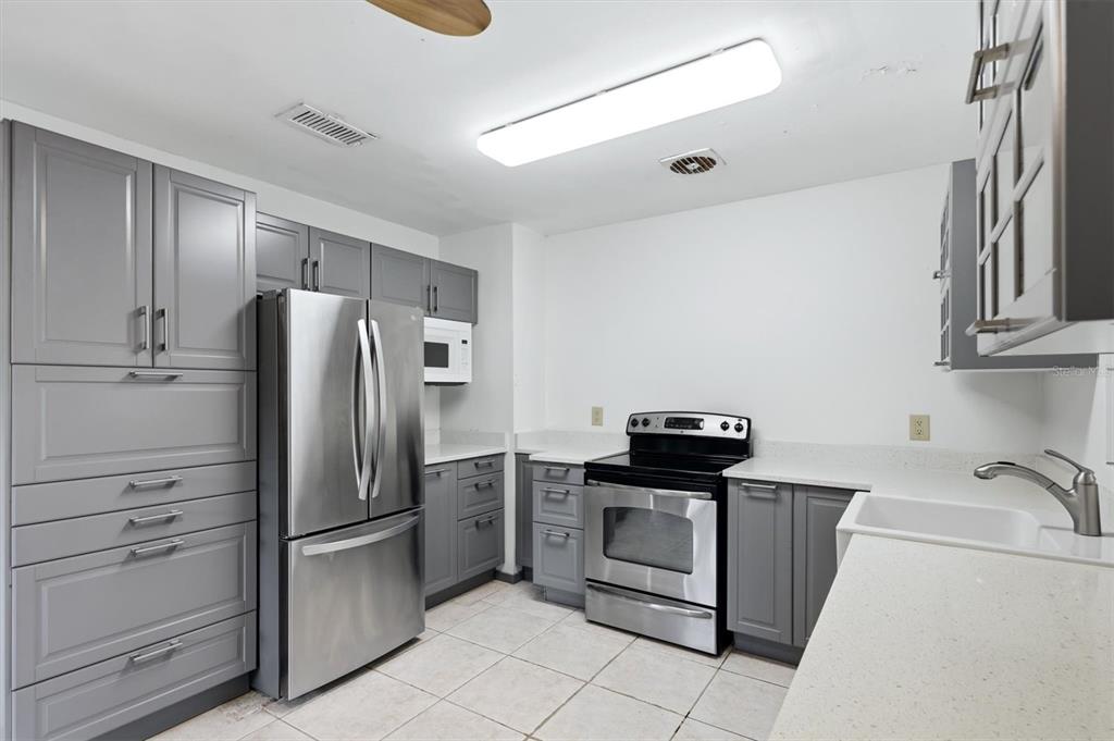 A kitchen features gray cabinets, stainless steel appliances, a farmhouse sink, and white countertops — 4003 BOOTH PLACE, SARASOTA, FL