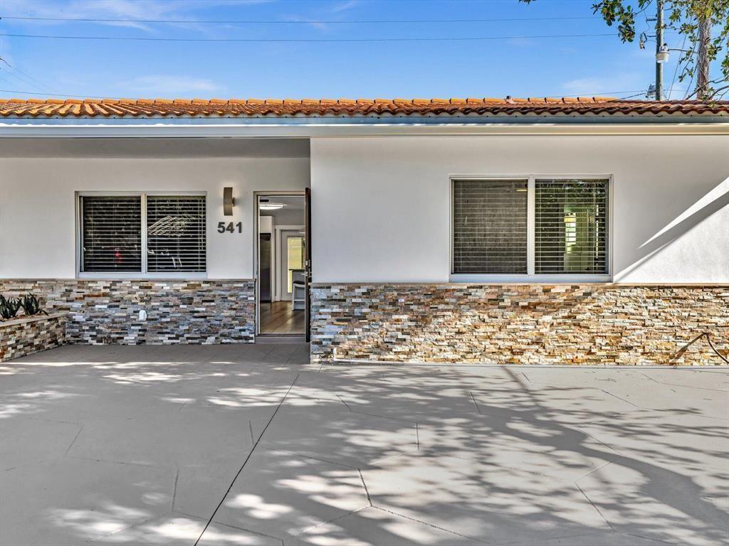 The exterior of a single-story house features white stucco walls and a stone veneer base — 541 NE 18th Street, Boca Raton FL 33432, BOCA RATON, FL