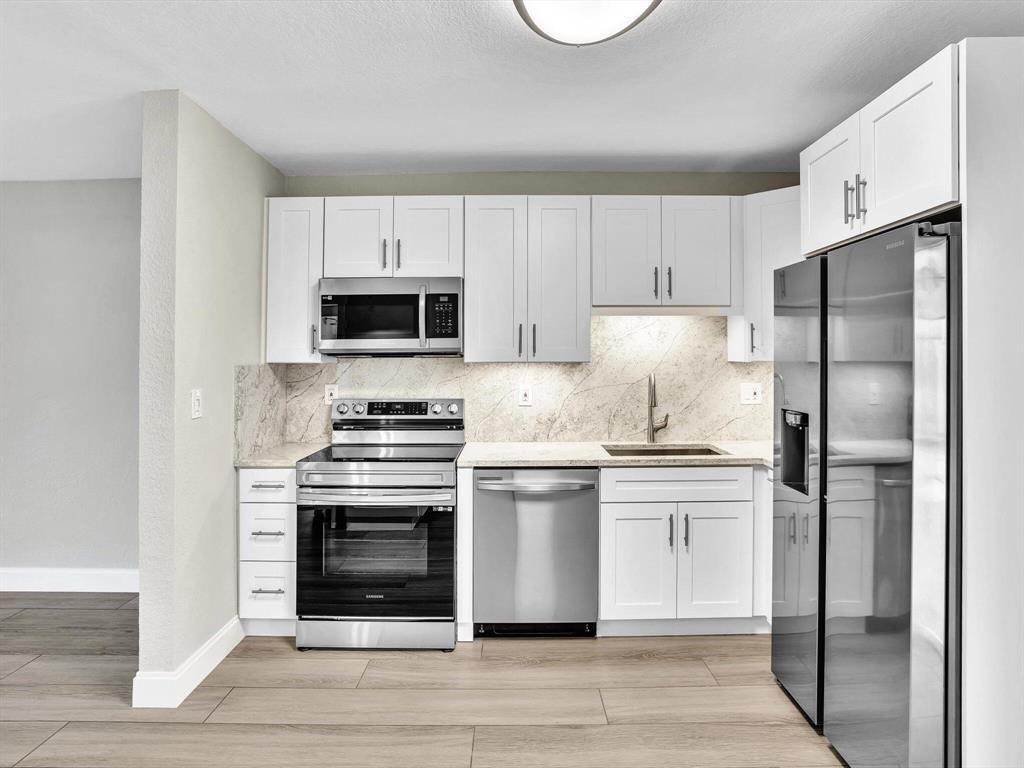 A modern kitchen features white cabinets, stainless steel appliances, and a marble-patterned backsplash — 541 NE 18th Street, Boca Raton FL 33432, BOCA RATON, FL