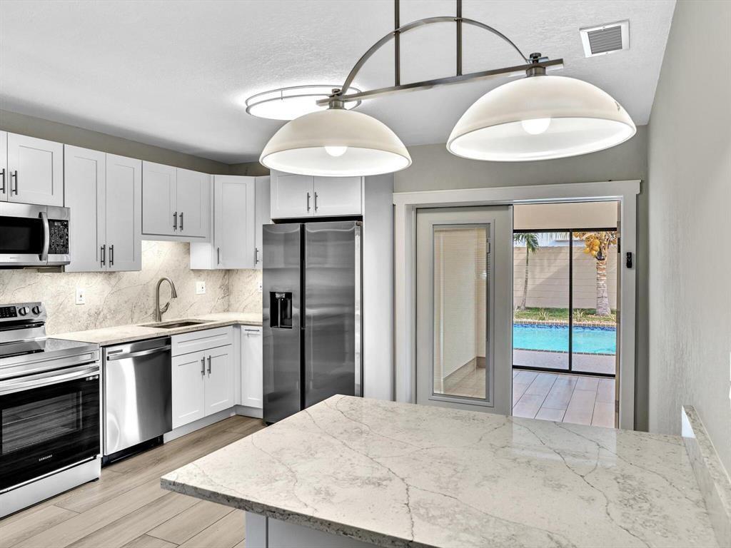 A modern kitchen features white cabinets, stainless steel appliances, marble-look countertops, and a pool view — 541 NE 18th Street, Boca Raton FL 33432, BOCA RATON, FL