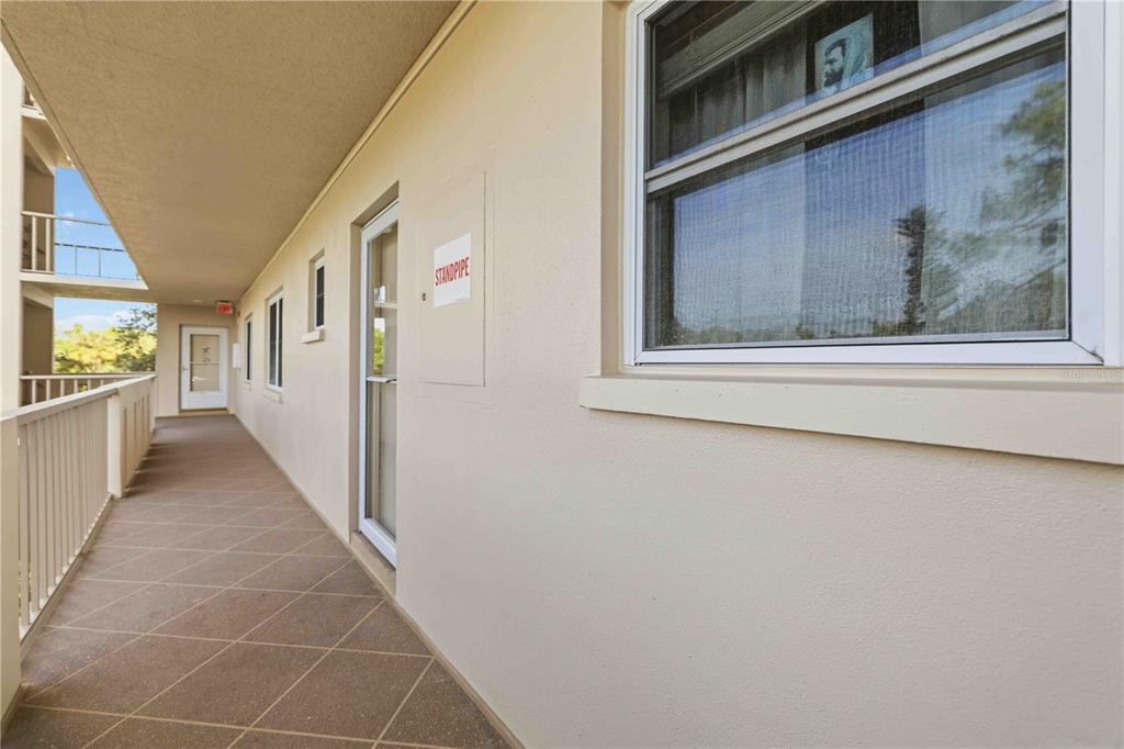 An exterior walkway with a tiled floor, white railing, and a standpipe access door — 3680 IRONWOOD CIRCLE UNIT 202L, BRADENTON, FL