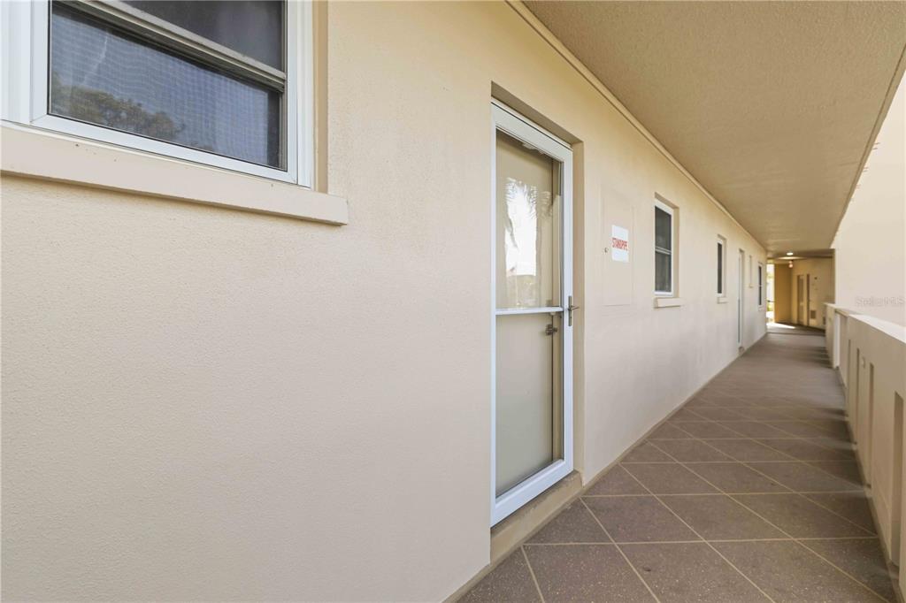 An exterior walkway with a white door and windows along a beige building wall — 3680 IRONWOOD CIRCLE UNIT 202L, BRADENTON, FL