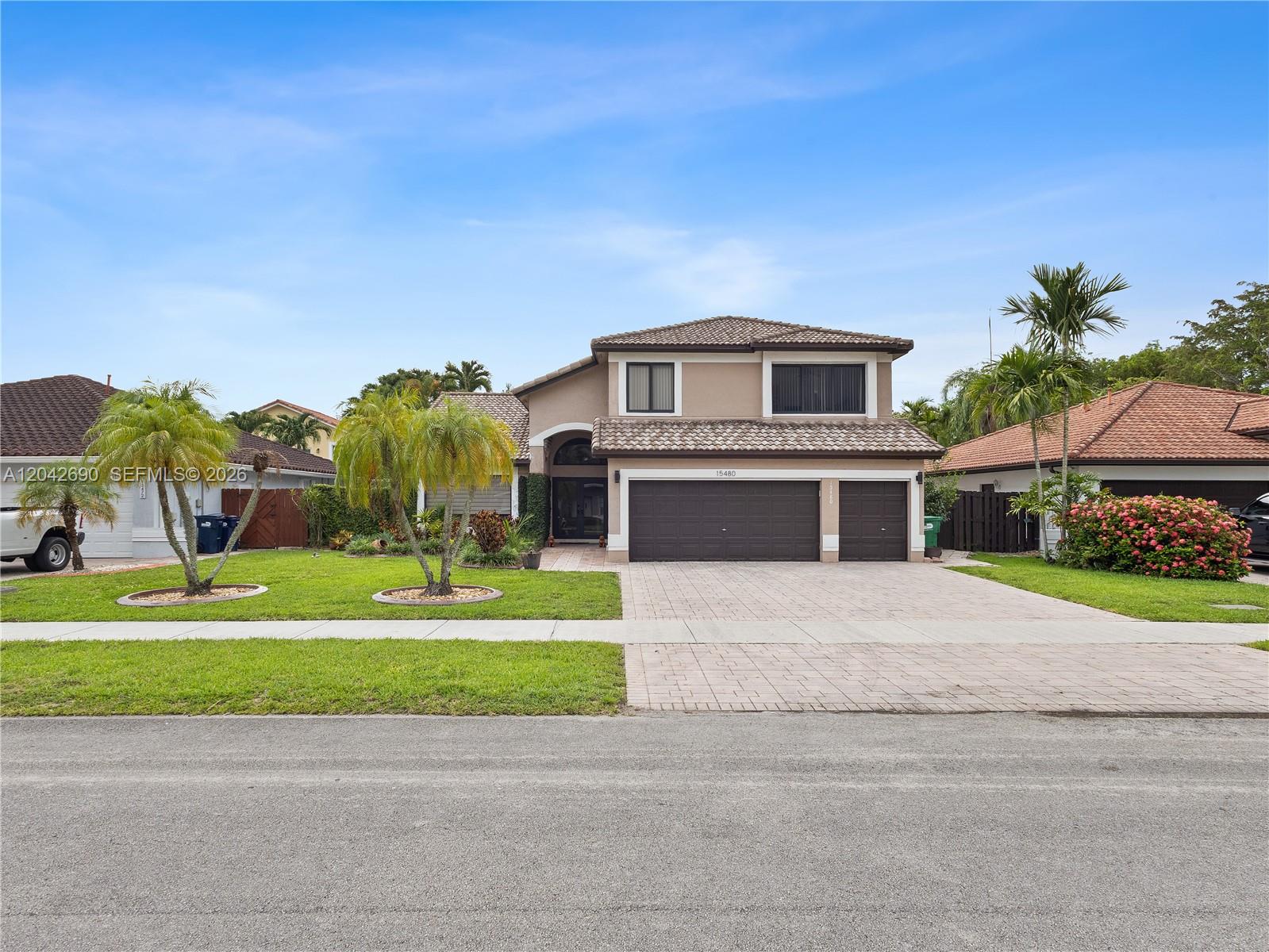 A backyard swimming pool with a waterfall feature sits beside a two-story tan house — 15480 SW 148th St, Miami FL 33196, MIAMI, FL