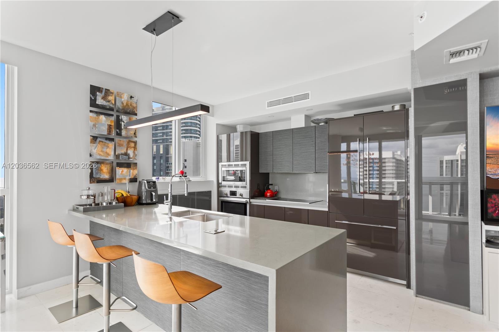 A modern kitchen features a gray island with bar stools and high-gloss cabinetry — 1080 Brickell Ave # 3300, Miami FL 33131, MIAMI, FL