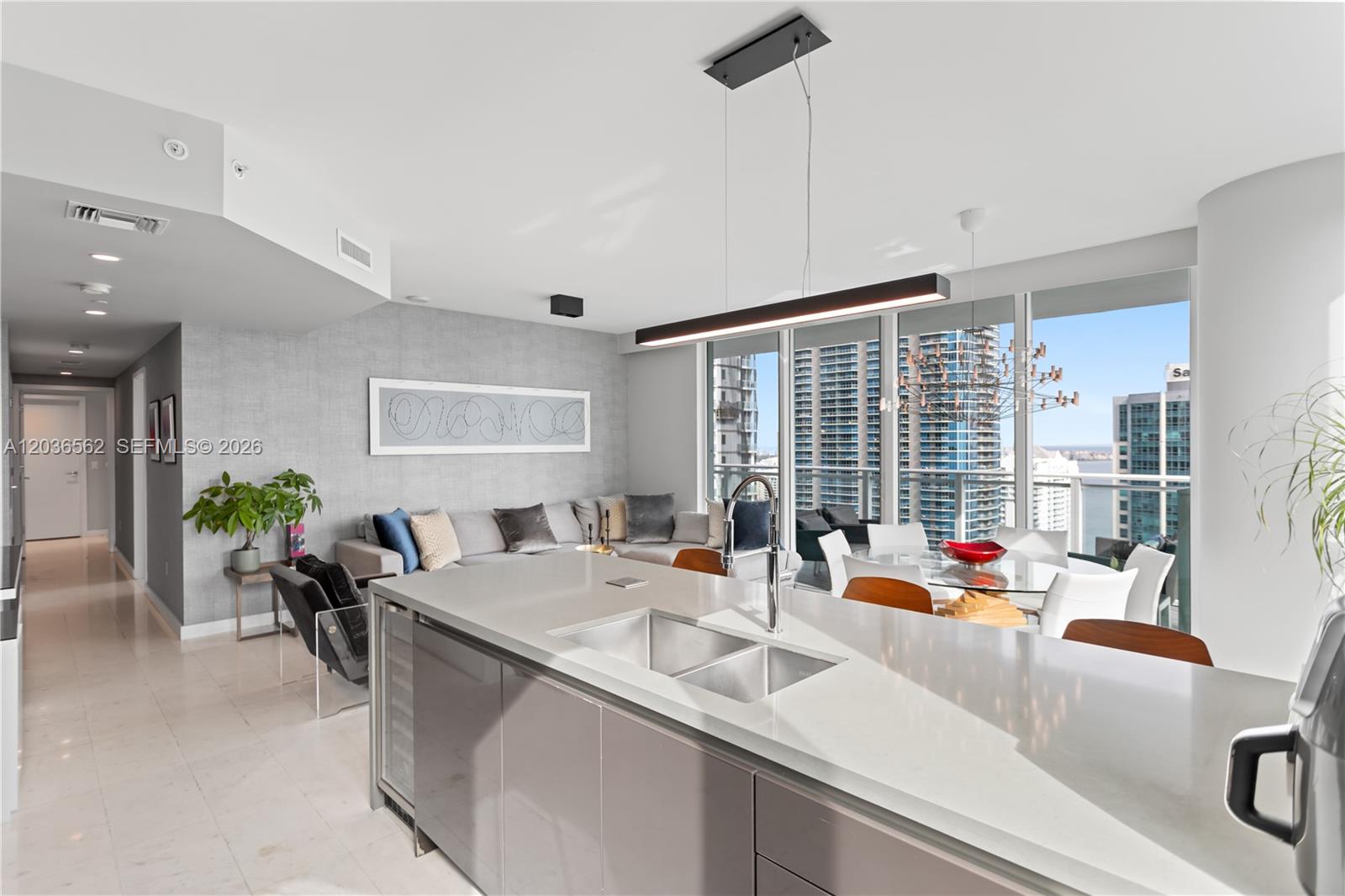 A modern kitchen island with a double sink overlooks a living area and dining space — 1080 Brickell Ave # 3300, Miami FL 33131, MIAMI, FL