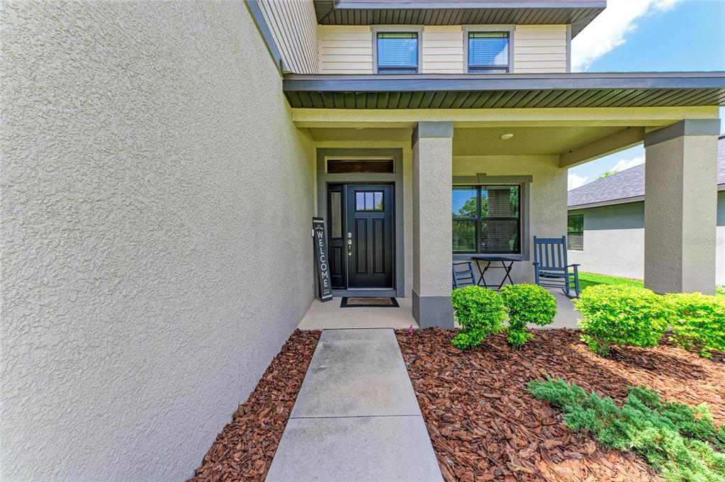 A concrete walkway leads to the covered front porch and black door of a house — 9507 43RD COURT E, PARRISH, FL