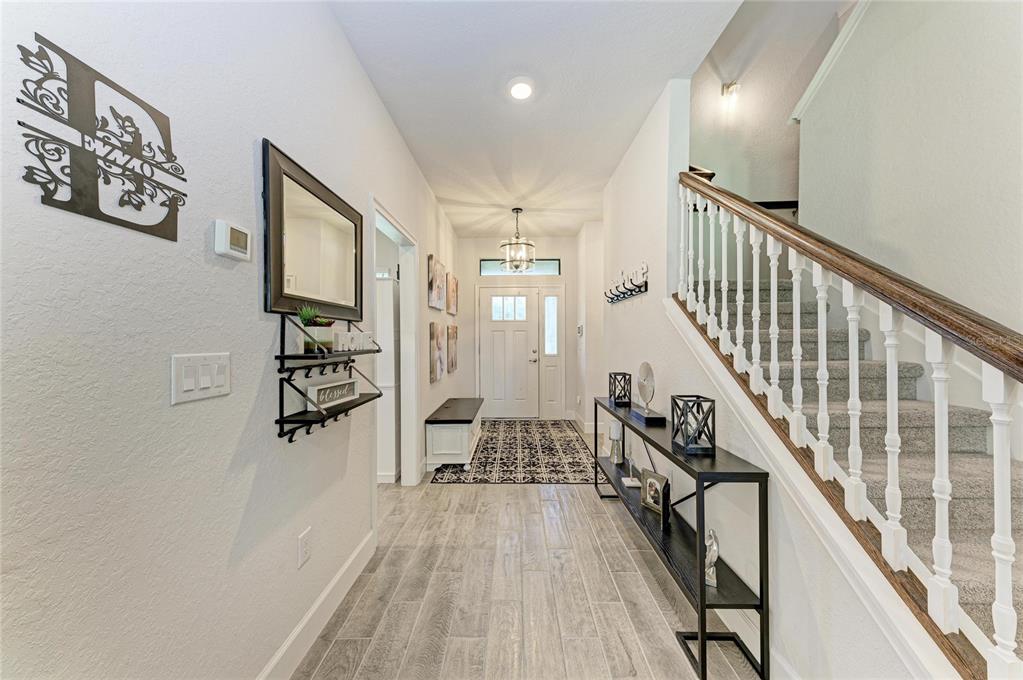 A bright entryway features wood-look tile flooring, a staircase with white railings, and a console table — 9507 43RD COURT E, PARRISH, FL