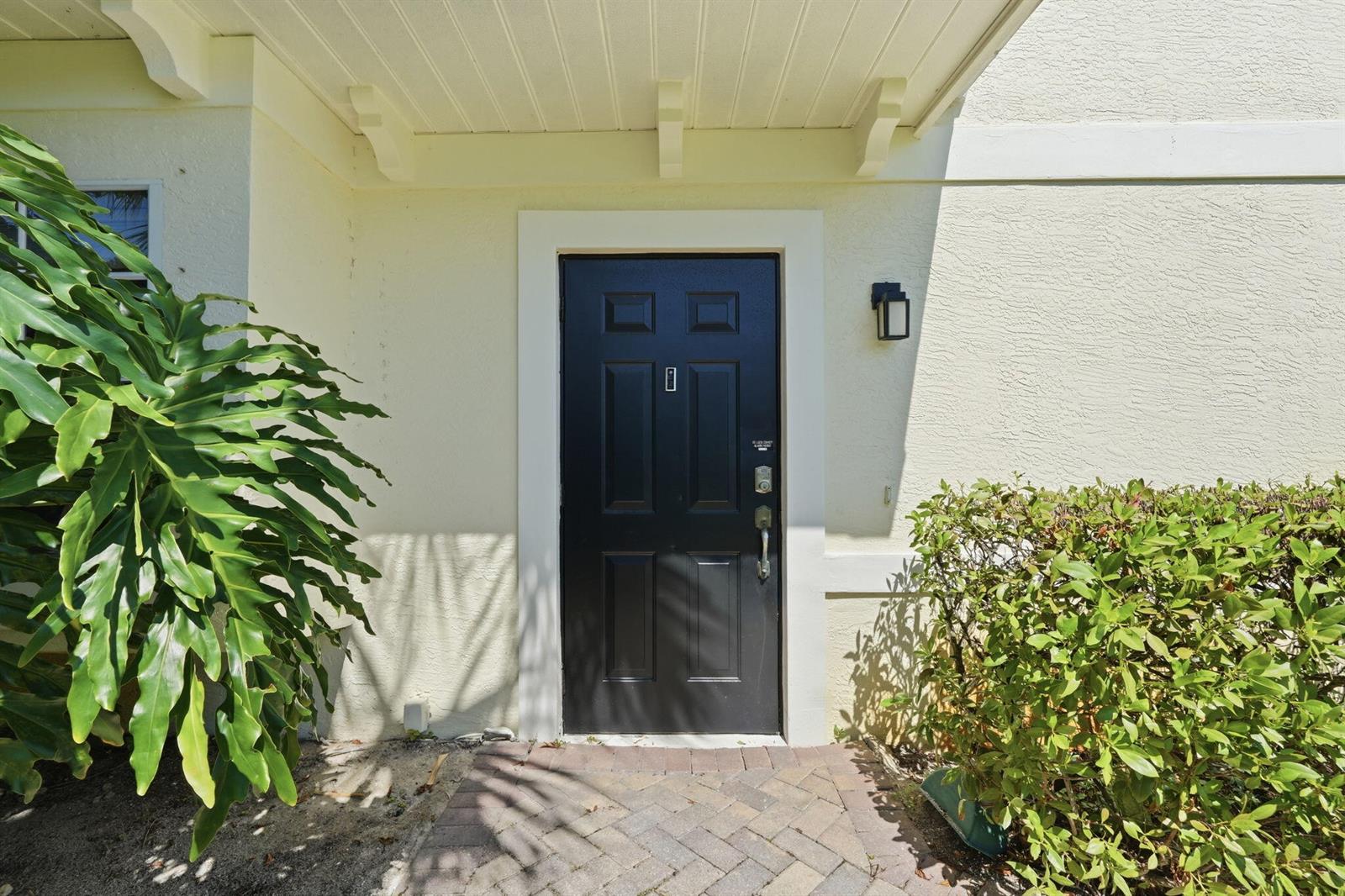 A black front door with a white frame is centered on a light-colored exterior wall — 2551 Creekside Drive, Fort Pierce FL 34981, FORT PIERCE, FL