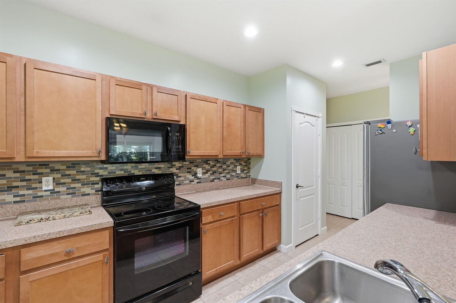 A kitchen features light wood cabinets, black appliances, a mosaic tile backsplash, and laminate countertops — 2551 Creekside Drive, Fort Pierce FL 34981, FORT PIERCE, FL