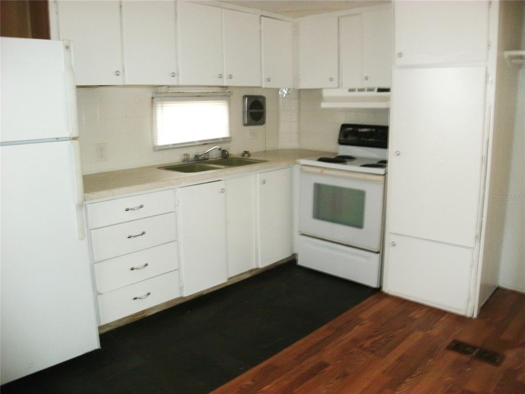 A kitchen features white cabinets, white appliances, a double sink, and dark flooring — 5410 TAYLOR AVENUE, PORT ORANGE, FL