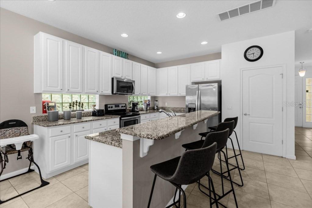 A kitchen features white cabinets, granite countertops, a breakfast bar with stools, and stainless appliances — 5220 OAKBOURNE AVENUE, DAVENPORT, FL