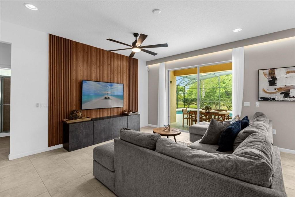 A living room features a wood-slat accent wall, a gray sectional sofa, and sliding glass doors — 5220 OAKBOURNE AVENUE, DAVENPORT, FL