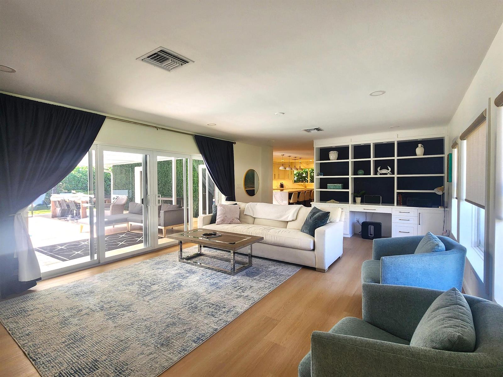 A bright living room features a white sofa, blue armchairs, built-in shelving, and sliding glass doors — 3481 NE 31st Avenue, Lighthouse Point FL 33064, LIGHTHOUSE POINT, FL