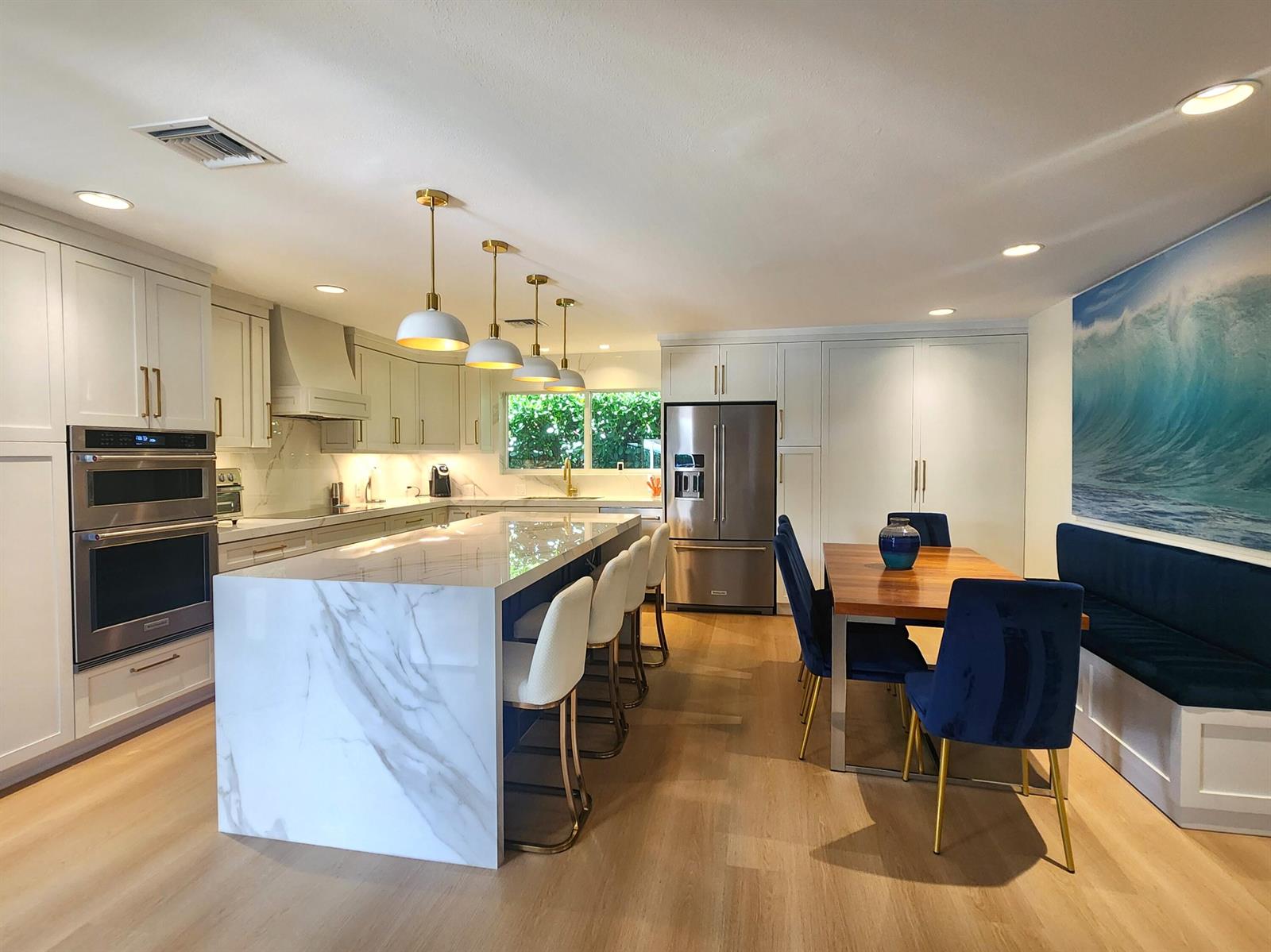 A modern kitchen features a marble waterfall island, white cabinetry, and a dining area — 3481 NE 31st Avenue, Lighthouse Point FL 33064, LIGHTHOUSE POINT, FL