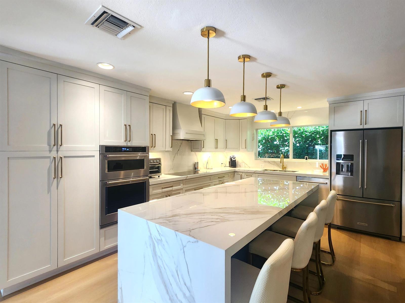 A modern kitchen features white cabinetry, a marble waterfall island, and four bar stools — 3481 NE 31st Avenue, Lighthouse Point FL 33064, LIGHTHOUSE POINT, FL