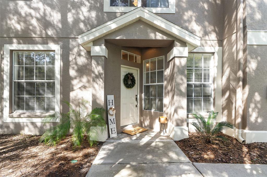 The exterior entrance of a home features a white front door, windows, and landscaping — 11269 WINDSOR PLACE CIRCLE, TAMPA, FL