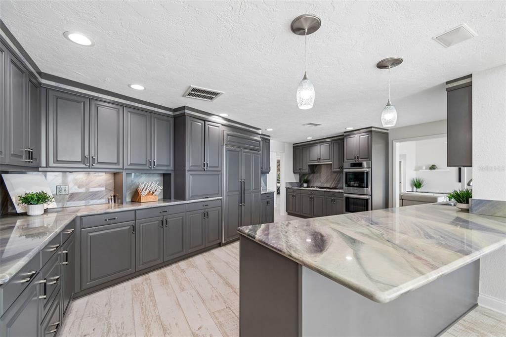 A modern kitchen features dark gray cabinetry, stone countertops, and light wood-look tile flooring — 2038 CAROLINA AVENUE NE, ST PETERSBURG, FL