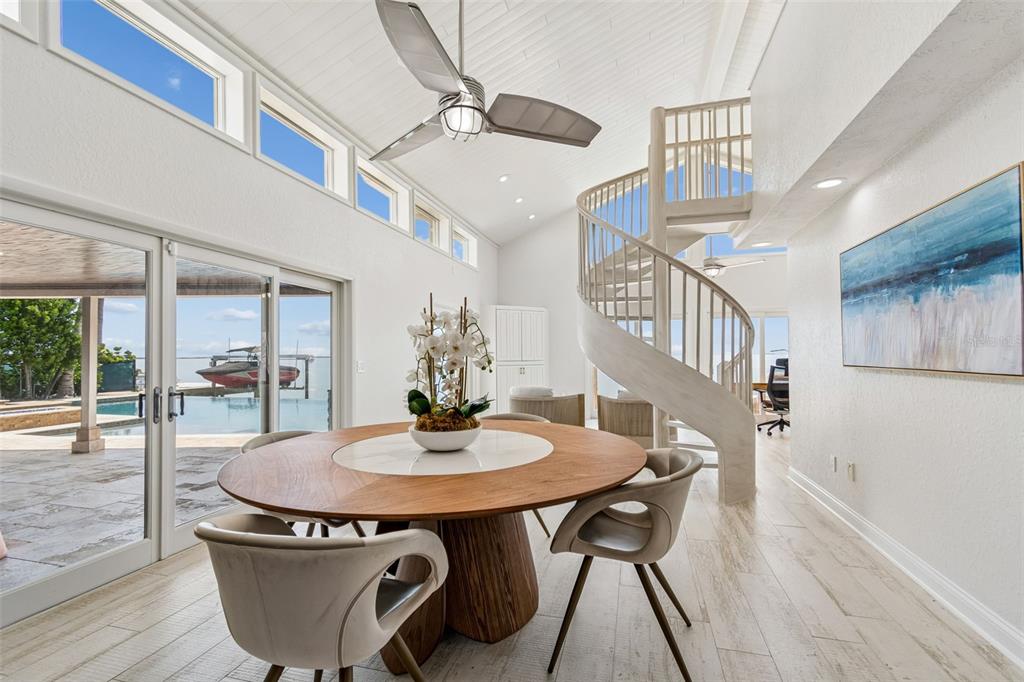 A dining area features a round wooden table, spiral staircase, and sliding doors overlooking water — 2038 CAROLINA AVENUE NE, ST PETERSBURG, FL