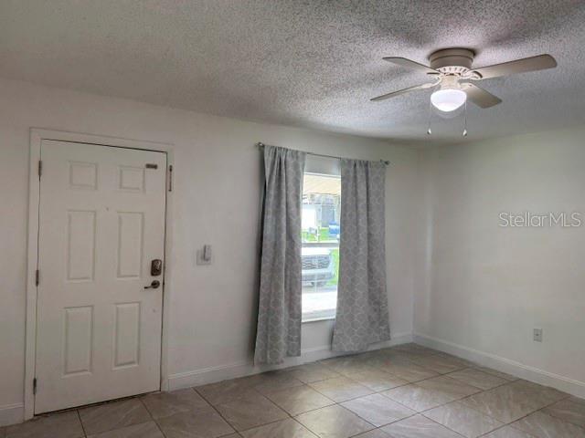 A room with a white door, tiled floor, ceiling fan, and window with gray curtains — 27127 FERNERY AVENUE, BROOKSVILLE, FL