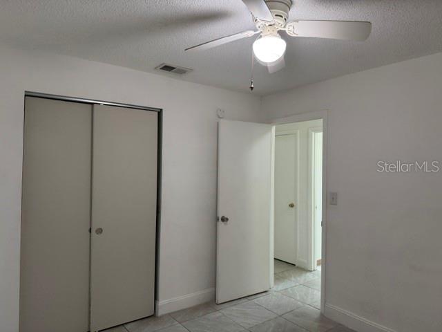 A bedroom with a ceiling fan, tiled flooring, a sliding closet door, and an open doorway — 27127 FERNERY AVENUE, BROOKSVILLE, FL