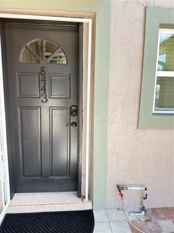 A dark gray front door with a keypad lock sits beside a beige stucco wall — 8443 N GRADY AVENUE, TAMPA, FL