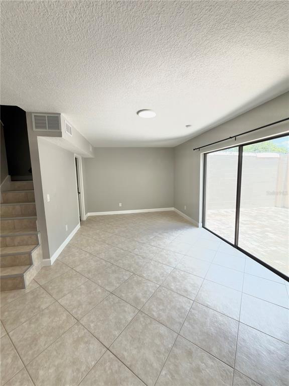 An empty room with light-colored tile flooring, gray walls, stairs, and a large sliding door — 8443 N GRADY AVENUE, TAMPA, FL
