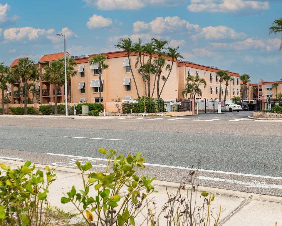 A multi-story peach-colored apartment building with palm trees and a parking lot in front — 8911 BLIND PASS ROAD UNIT 220, ST PETE BEACH, FL