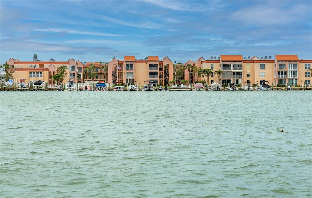 A multi-story waterfront apartment complex features a row of boat slips along the shore — 8911 BLIND PASS ROAD UNIT 220, ST PETE BEACH, FL