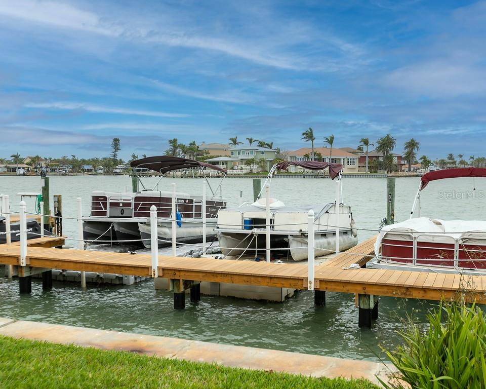 Three pontoon boats are docked at a wooden pier on a calm waterway — 8911 BLIND PASS ROAD UNIT 220, ST PETE BEACH, FL